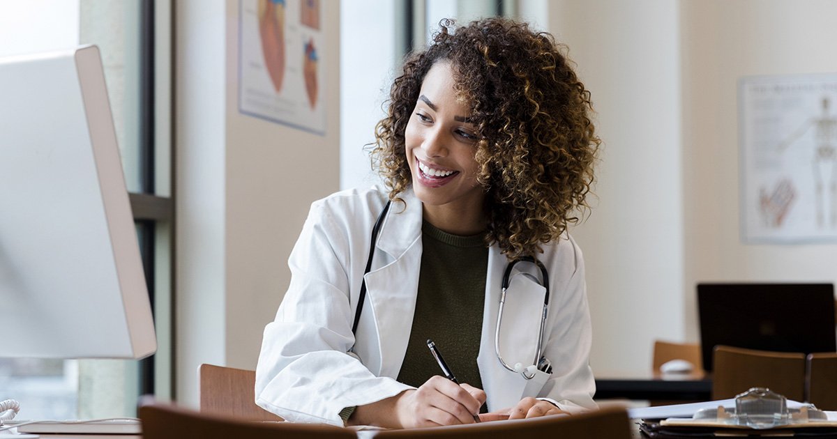 physician working at desk and looking at computer display while taking notes physician working at desk and looking at computer display while taking notes